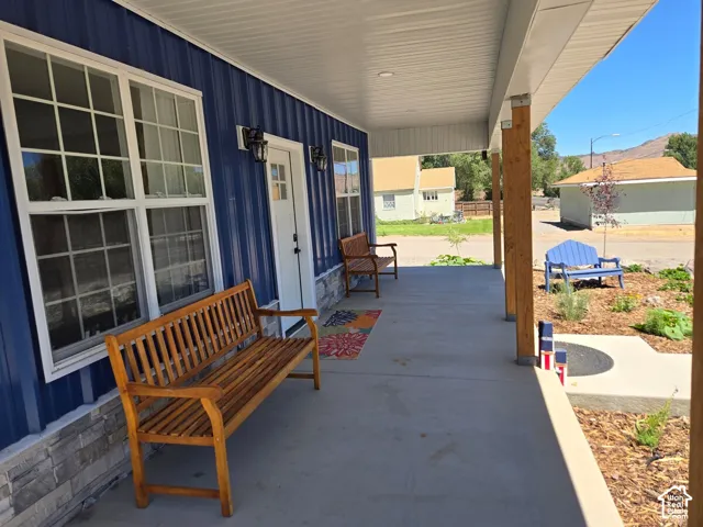 Covered front porch featuring vertical blue metal siding, stone veneer base, grid-pattern windows, and natural wood support columns