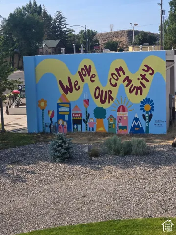 Exterior masonry wall featuring a painted mural, gravel landscaping, and mature shrubbery