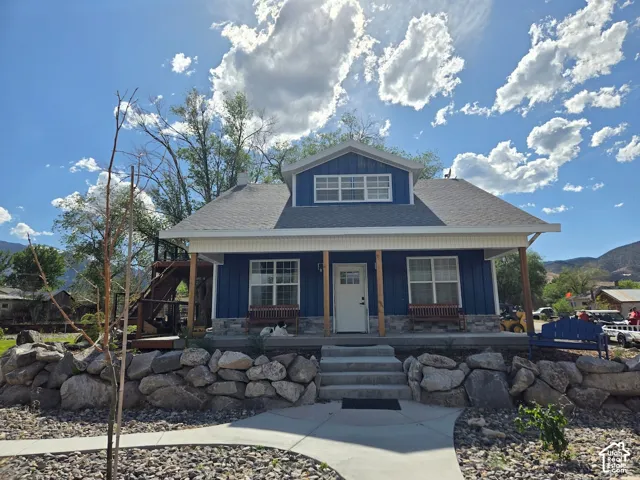 Blue board-and-batten siding with stone veneer foundation, covered front porch with timber support posts, concrete staircase, and tiered natural stone retaining wall