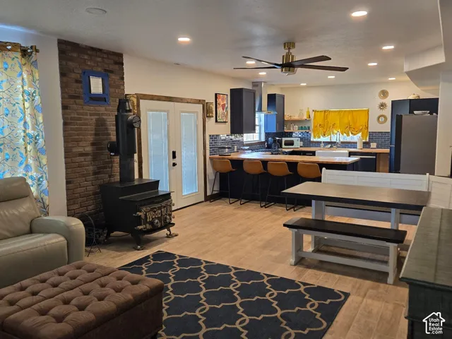 Open-concept kitchen featuring dark cabinetry, butcher block countertops, an apron-front sink, wood-finish flooring, and a floor-to-ceiling brick accent wall with a wood-burning stove