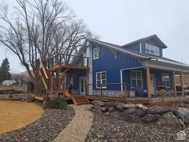 Vertical blue metal siding exterior featuring a stone veneer foundation, multi-level wood deck, metal stair railing, and a covered porch
