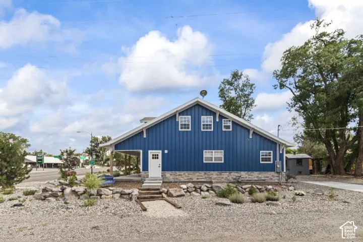 Exterior featuring blue board-and-batten siding, stone veneer foundation, metal-roofed covered porch, and rock-lined landscaping