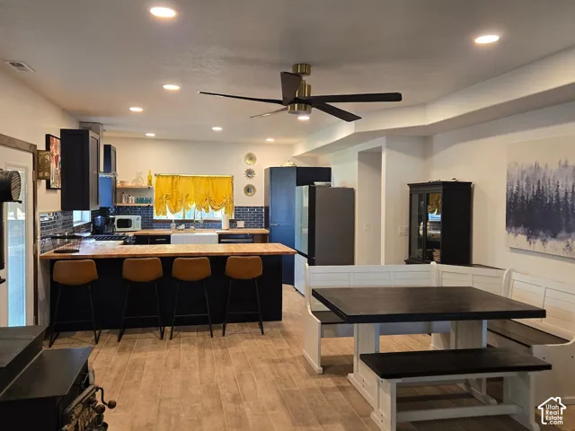 Kitchen featuring dark cabinetry, butcher block countertops, a farmhouse-style sink, wood-finish tile flooring, and recessed lighting