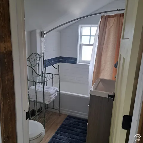 Bathroom featuring wood-finish flooring, a white porcelain tub with white subway tile surround, a blue tile accent band, and a single-basin vanity