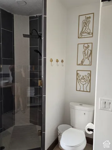 Walk-in glass-enclosed shower featuring dark vertical tile surround and rainfall showerhead, complemented by wall-mounted gold-toned hardware