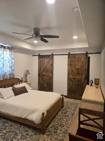 Tray ceiling with recessed lighting, dual sliding barn-style doors with black hardware, and wood-finish flooring