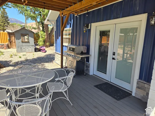 Covered deck featuring composite decking, vertical metal siding, stone veneer accents, and double glass-pane doors