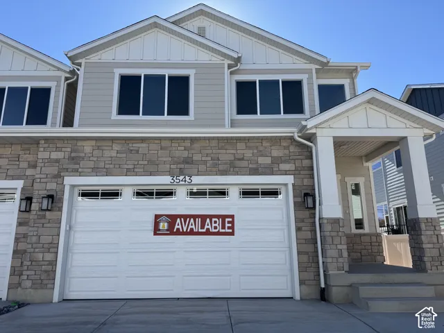 Exterior featuring mixed-material siding and stone veneer, double-car garage with transom windows, covered entryway, and concrete porch