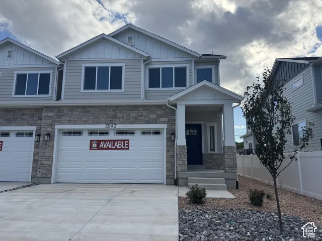 Multi-story exterior featuring stone veneer siding, horizontal lap siding, white trim detailing, a covered entryway, and a two-car garage