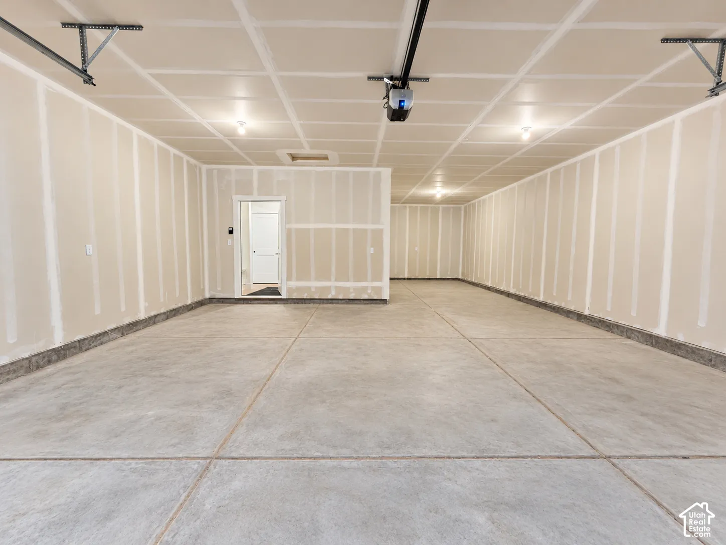Finished garage featuring concrete flooring, taped and mudded drywall, overhead lighting, and an automatic garage door opener