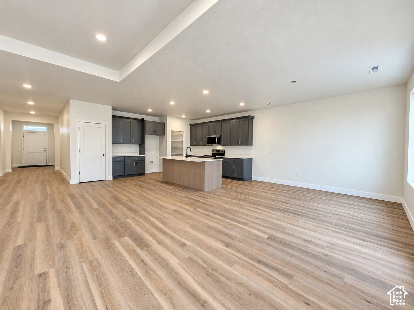 Open-concept interior featuring wood-finish flooring, recessed lighting, a center kitchen island with quartz countertops, dark shaker-style cabinetry, and a walk-in pantry