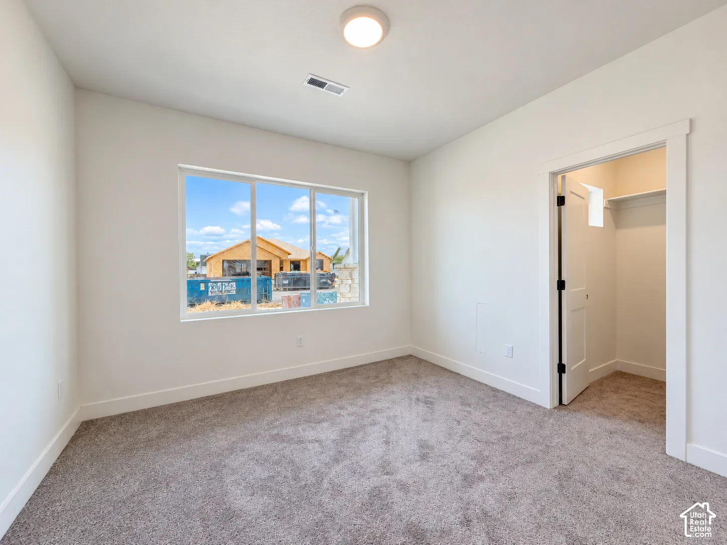 Room featuring neutral carpeting, a large picture window, a flush-mount ceiling light, and an interior closet with built-in shelving