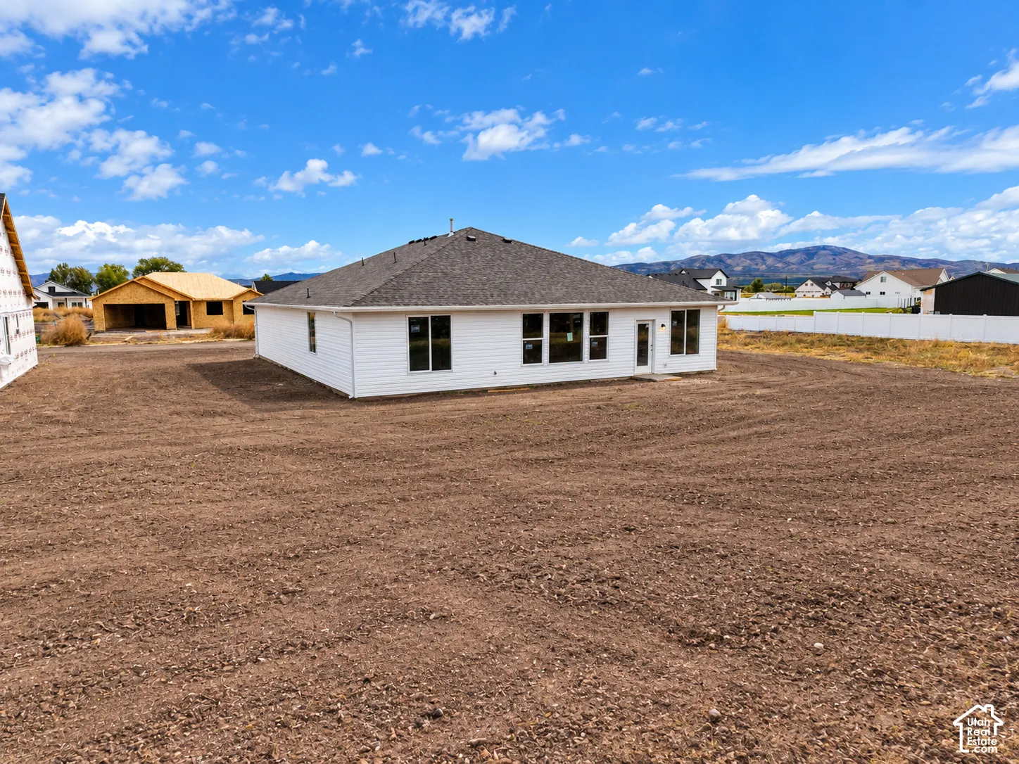 Single-story residence featuring white horizontal siding, a hipped roof with asphalt shingles, expansive open lot, and mountain backdrop