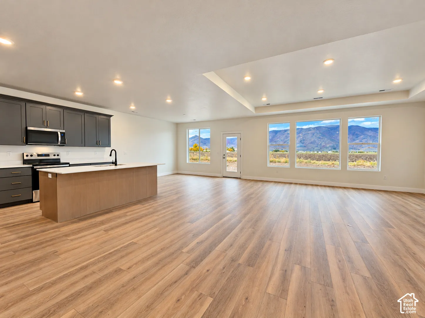 Open-concept space featuring wood-finish flooring, recessed lighting, a kitchen with dark cabinetry, a central island with a solid-surface countertop, and expansive windows with mountain scenery