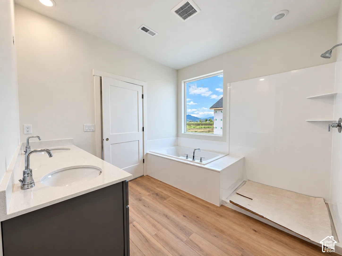 Bathroom featuring wood-finish flooring, a quartz countertop vanity with an oval undermount sink, a deep soaking tub, and a separate stall shower with integrated shelving