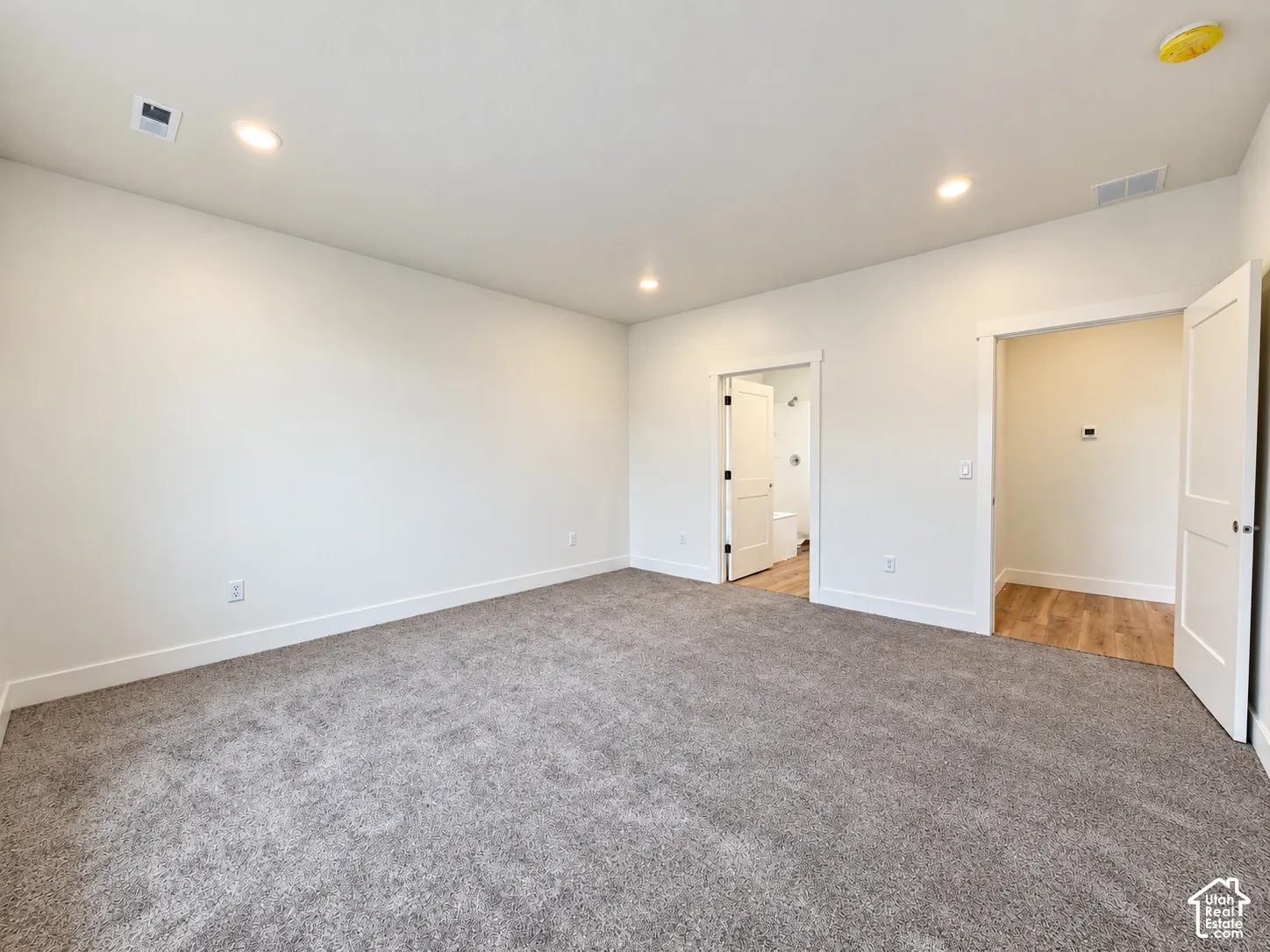 Neutral-toned carpeting, recessed ceiling lighting, two-panel interior doors, and wood-finish flooring in the threshold areas