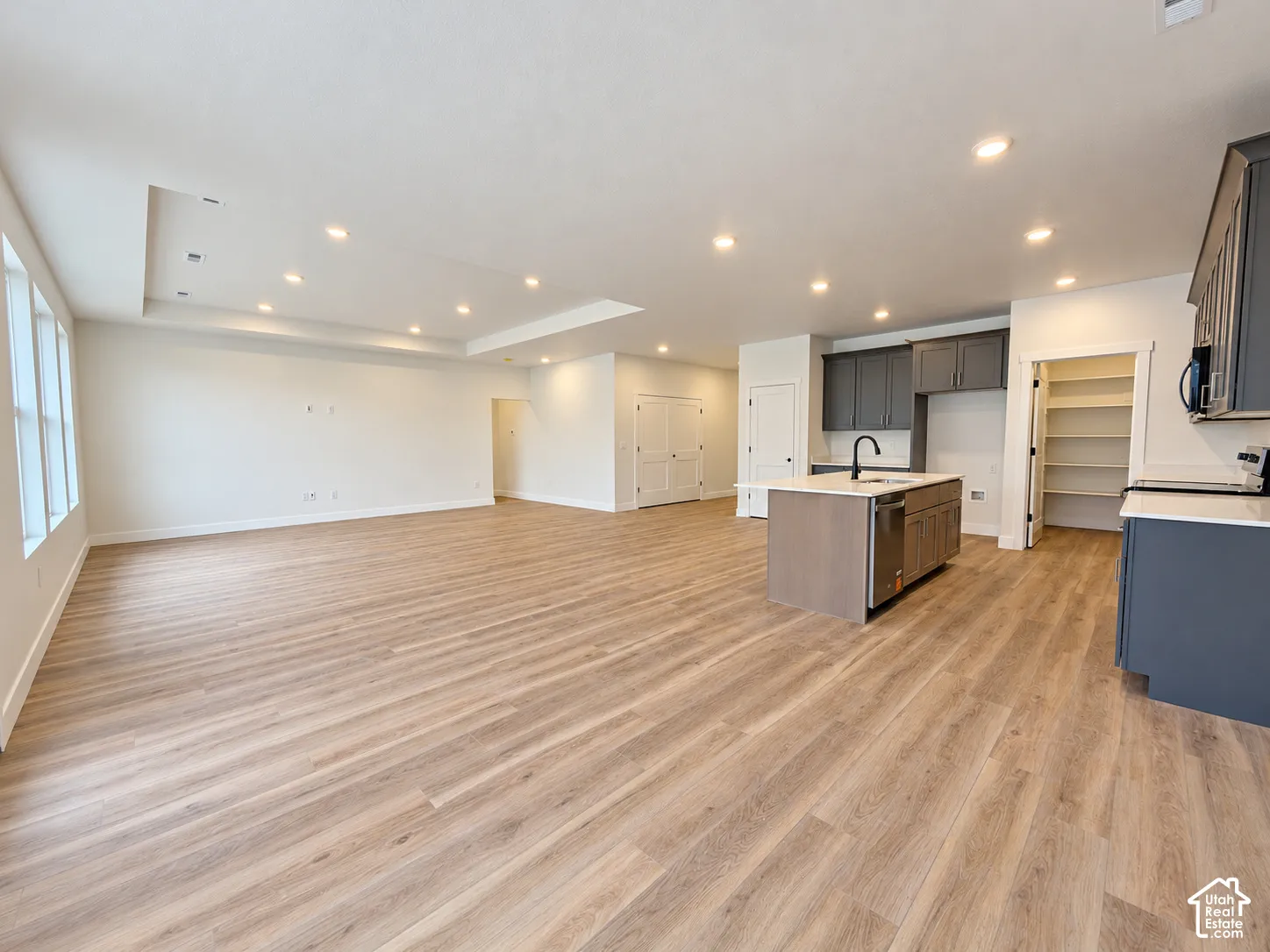 Open-concept interior featuring wood-finish flooring, recessed lighting, a center island with a stone countertop, dark cabinetry, and an integrated pantry with built-in shelving