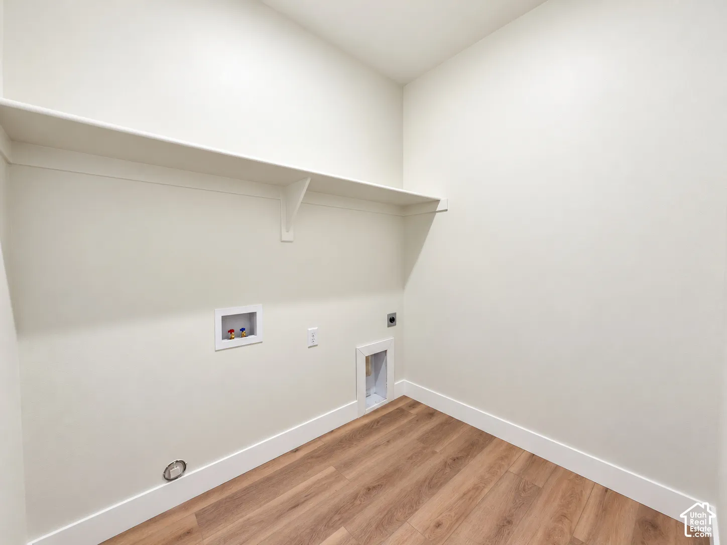 Utility space featuring wood-finish flooring, a wall-mounted shelving unit, and dedicated hookups for laundry appliances