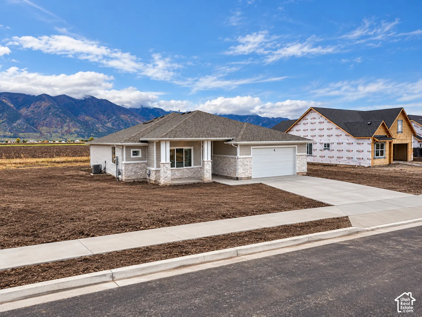 Single-level residence featuring a stone-veneer facade, multi-gabled roofline, concrete driveway, and mountain backdrop