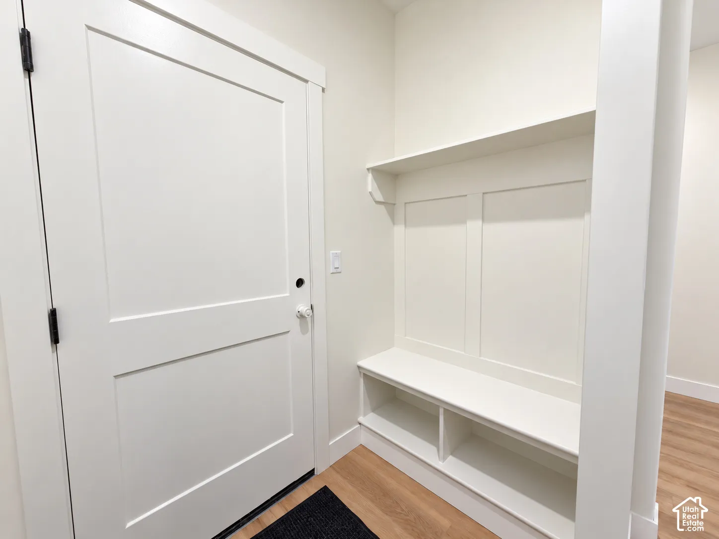 Built-in entryway storage bench featuring shaker-style millwork, open lower shelving, an upper display shelf, and wood-finish flooring