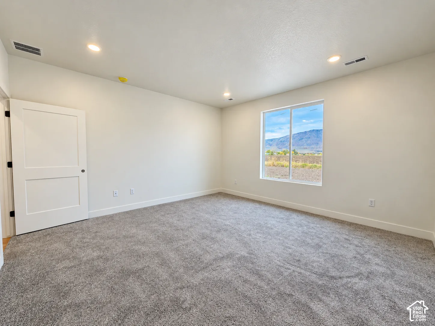 Neutral interior space featuring high-pile carpeting, recessed lighting, a single-panel interior door, and a window providing a mountain backdrop