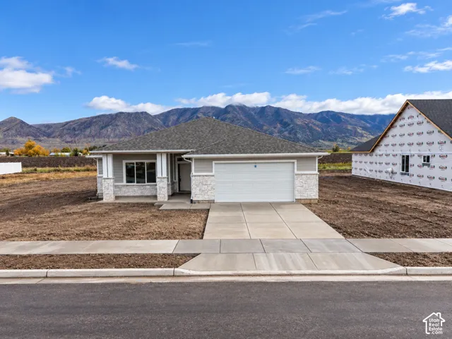 Single-level residence featuring a stone and horizontal siding exterior, covered front porch, attached two-car garage, and concrete driveway set against a mountain backdrop