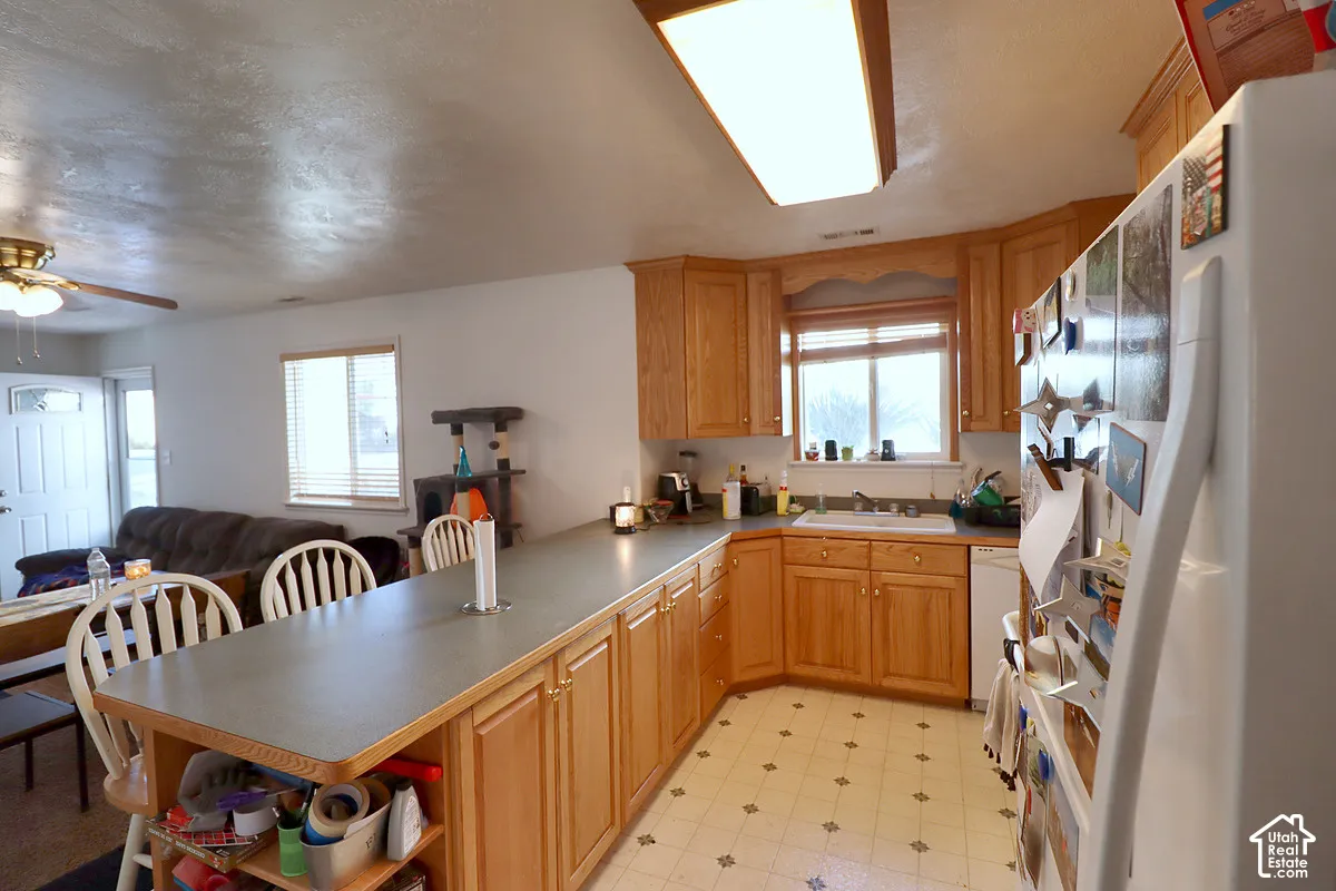 Kitchen featuring natural wood cabinetry, solid-surface countertops, extended breakfast bar, inset sink with faucet, and recessed lighting
