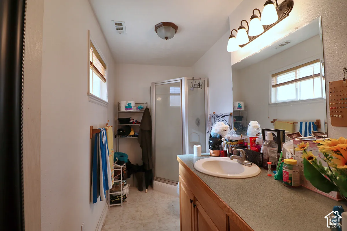 Bathroom featuring a vanity with an integrated basin, a large wall-mounted mirror, a four-light fixture, and a corner shower enclosure with a glass door