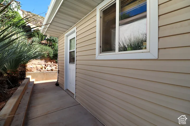 Exterior siding featuring horizontal lap panels, a single-lite white entry door, concrete walkway, and tiered rock-retaining wall