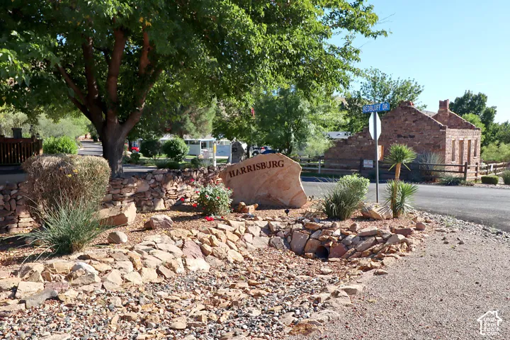 Community signage featuring a natural stone monument, stone retaining wall, xeriscaped ground cover, and mature trees