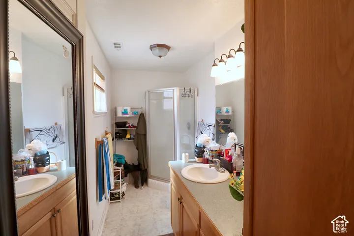 Bathroom featuring a wood-finish vanity with a stone-composite countertop, integrated oval sink, glass-enclosed corner shower, and a multi-bulb light fixture