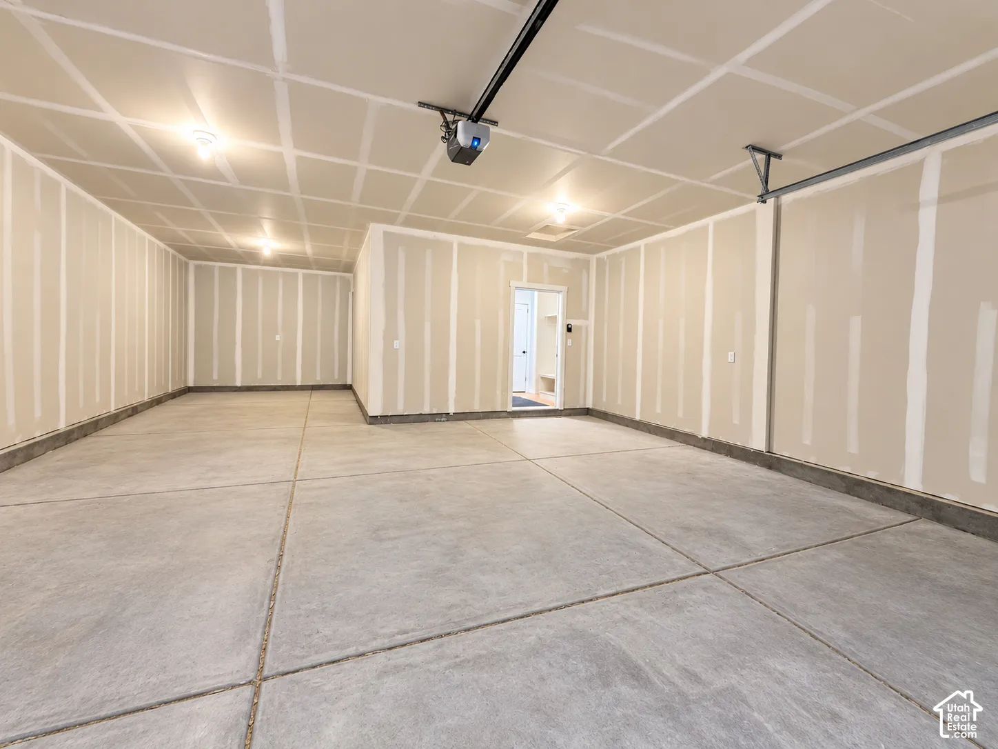Spacious garage featuring finished drywall walls and ceiling, concrete flooring, and an automated overhead door opener
