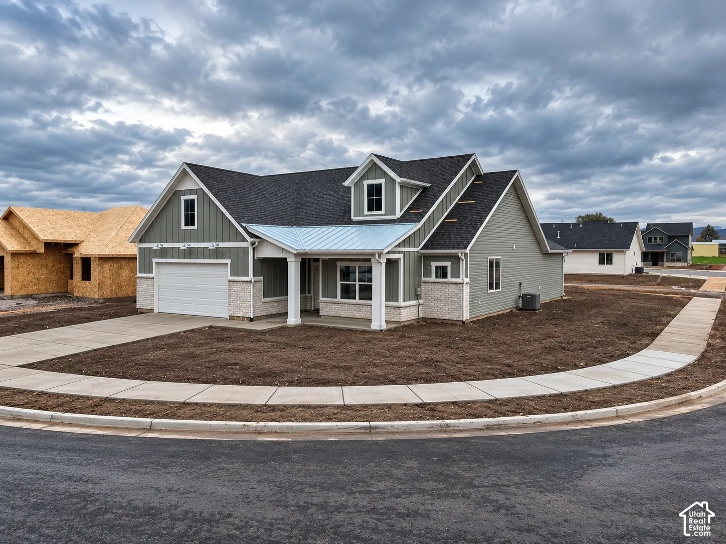Single-level exterior featuring a combination of horizontal lap siding and stone veneer, a metal-accented roof over the entryway, a gabled roofline with a dormer window, and a two-car garage