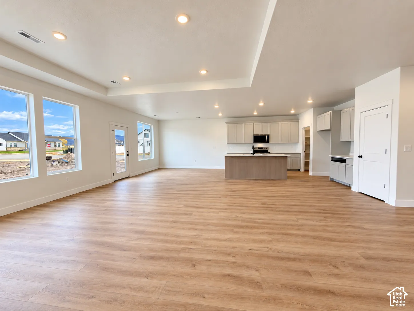 Open-concept interior featuring wood-finish flooring, recessed lighting, a tray ceiling, and a kitchen equipped with a central island and light-toned cabinetry