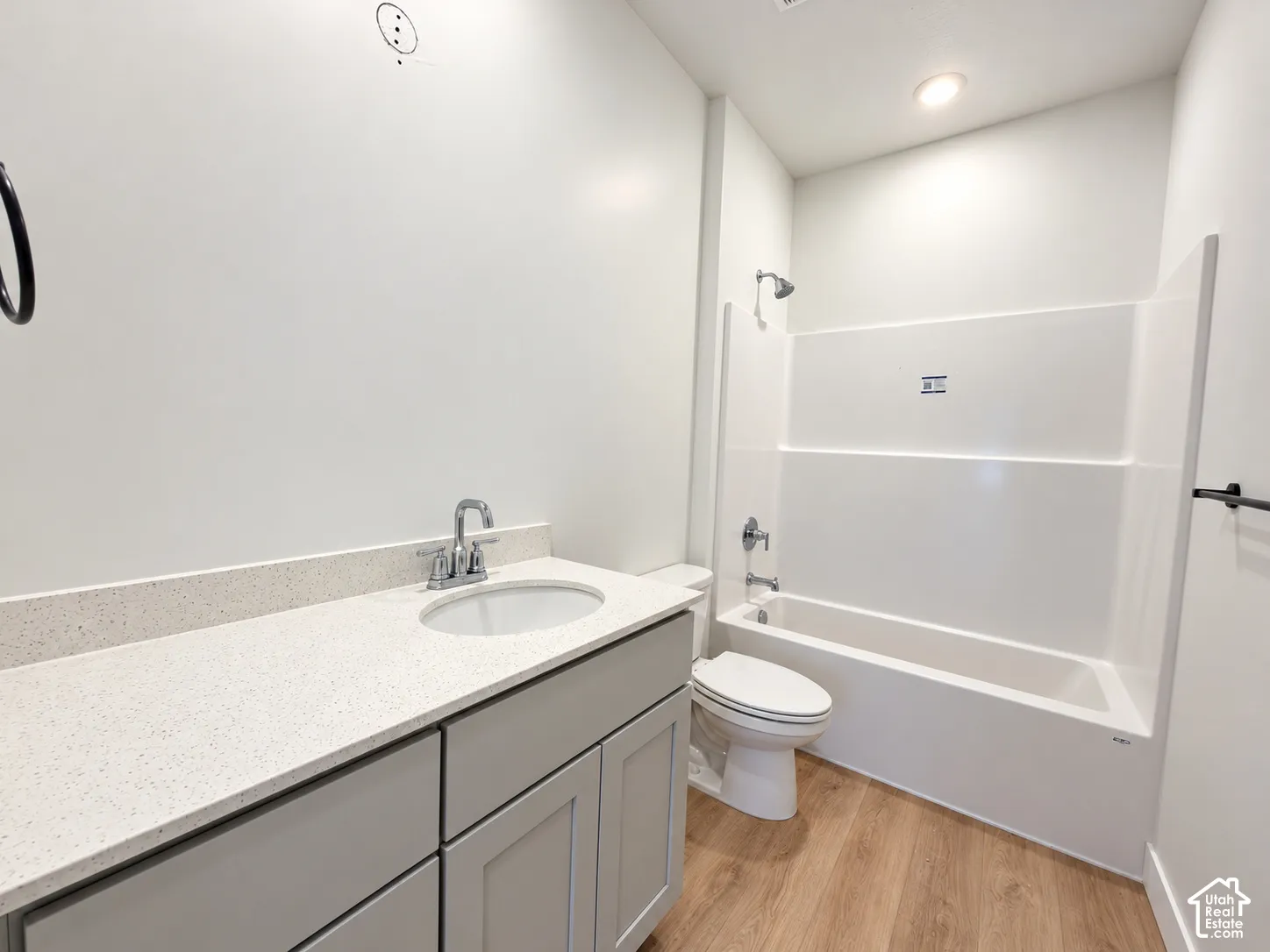 Bathroom featuring a light gray vanity with a stone-composite countertop, integrated sink, wood-finish flooring, and a white tub-shower combination with chrome hardware