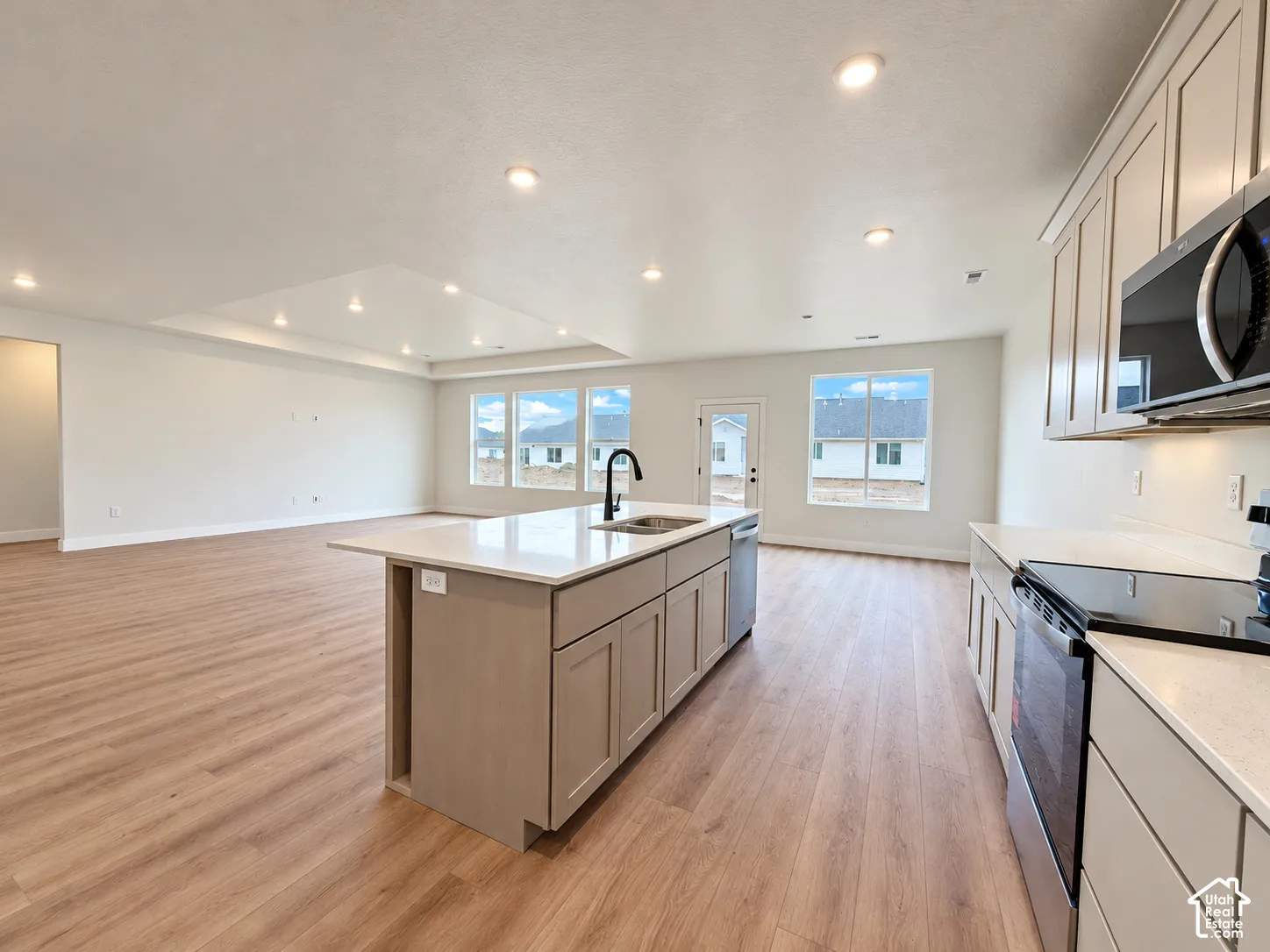 Open-concept kitchen featuring an island with a quartz countertop and undermount sink, recessed lighting, wood-finish flooring, and shaker-style cabinetry