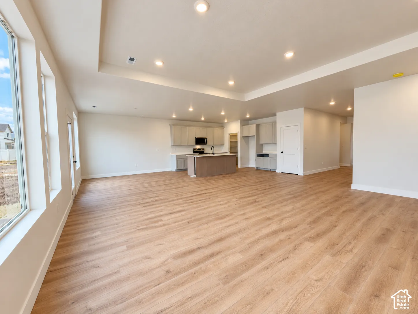 Open-concept interior featuring wood-finish flooring, recessed lighting, a tray ceiling, and a kitchen equipped with cabinetry and a center island