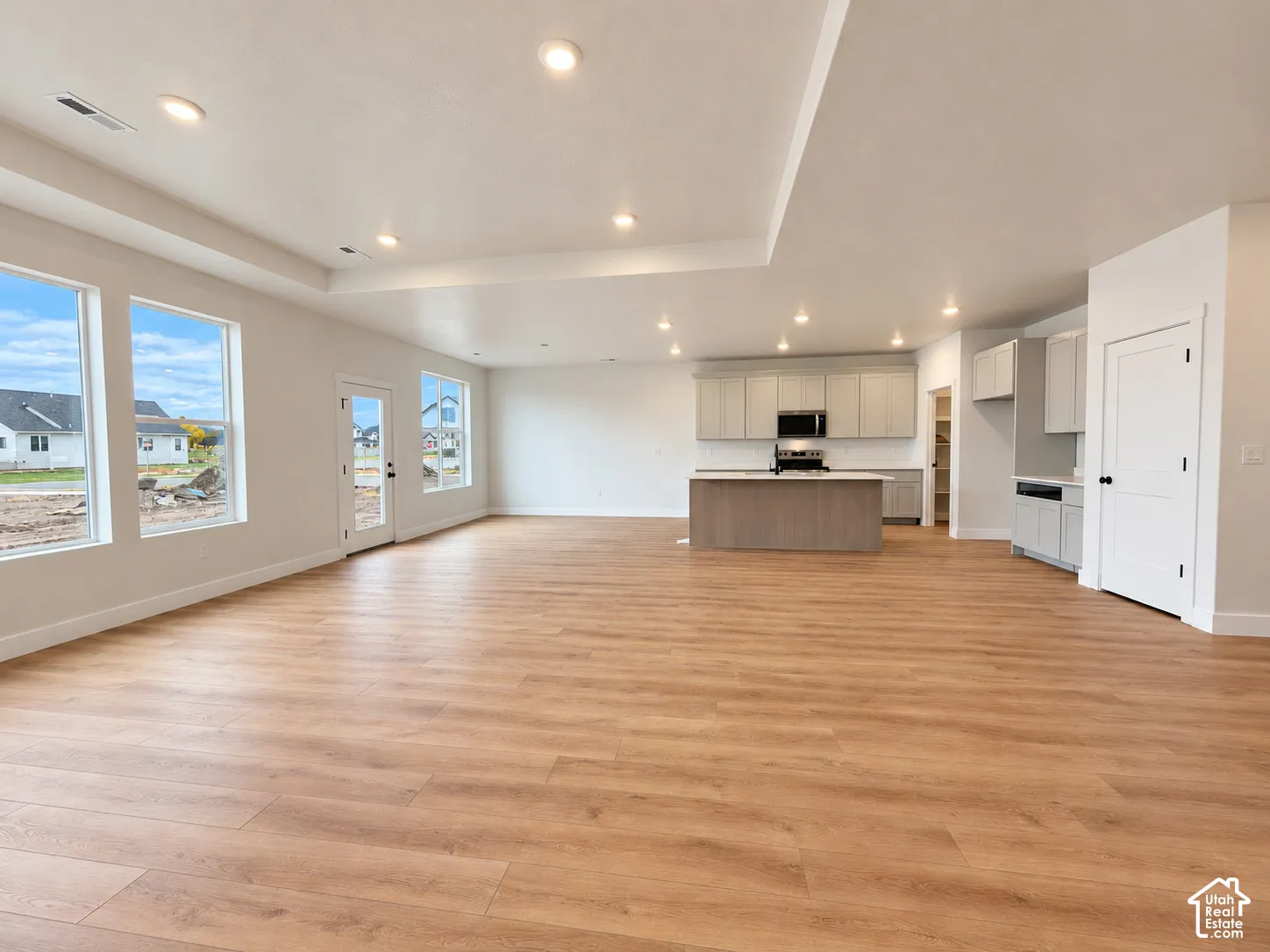 Open-concept area featuring wood-finish flooring, recessed lighting, tray ceiling, central kitchen island, and shaker-style cabinetry