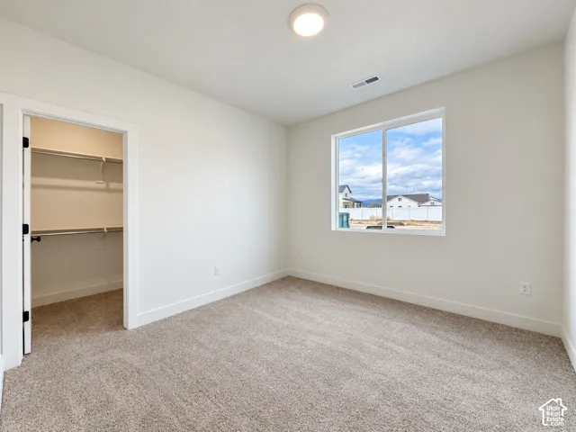 Neutral-toned interior featuring wall-to-wall carpeting, a large sliding window, and a walk-in closet with built-in metal shelving