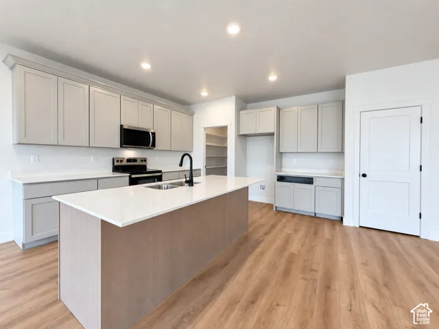 Kitchen featuring light-colored cabinetry, stone-finish countertops, a central island with an integrated stainless steel sink and matte black faucet, recessed lighting, and wood-finish flooring
