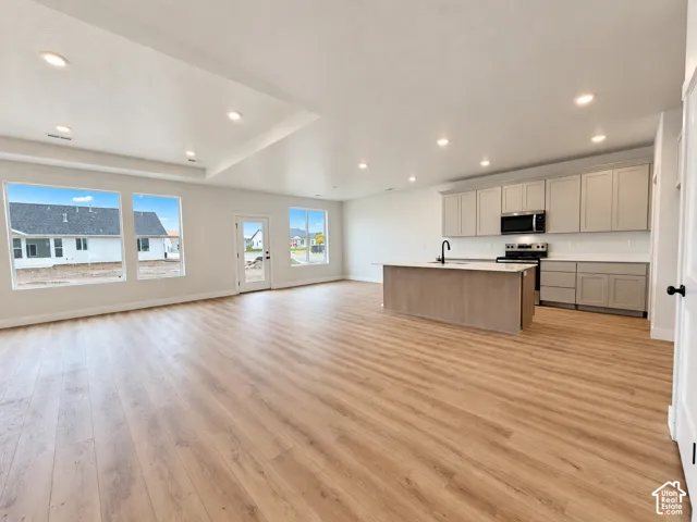 Open-concept space featuring wood-finish flooring, recessed lighting, a center island with a stone-finish countertop, neutral-tone cabinetry, and large windows