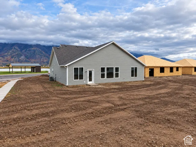 Single-story residence featuring light grey horizontal siding, asphalt shingle roofing, and a concrete walkway, set against a prominent mountain backdrop
