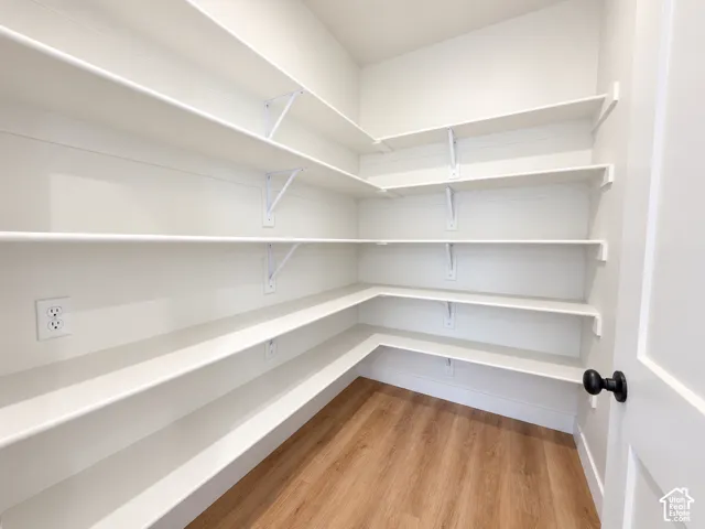 Walk-in pantry featuring white wrap-around shelving, wood-finish flooring, and electrical outlets