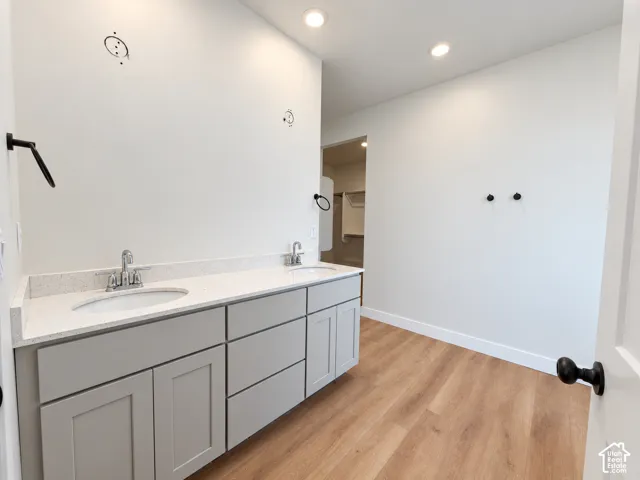 Dual-sink vanity featuring light-toned cabinetry, quartz countertops, integrated undermount sinks, and matte black hardware complemented by wood-finish flooring and recessed lighting