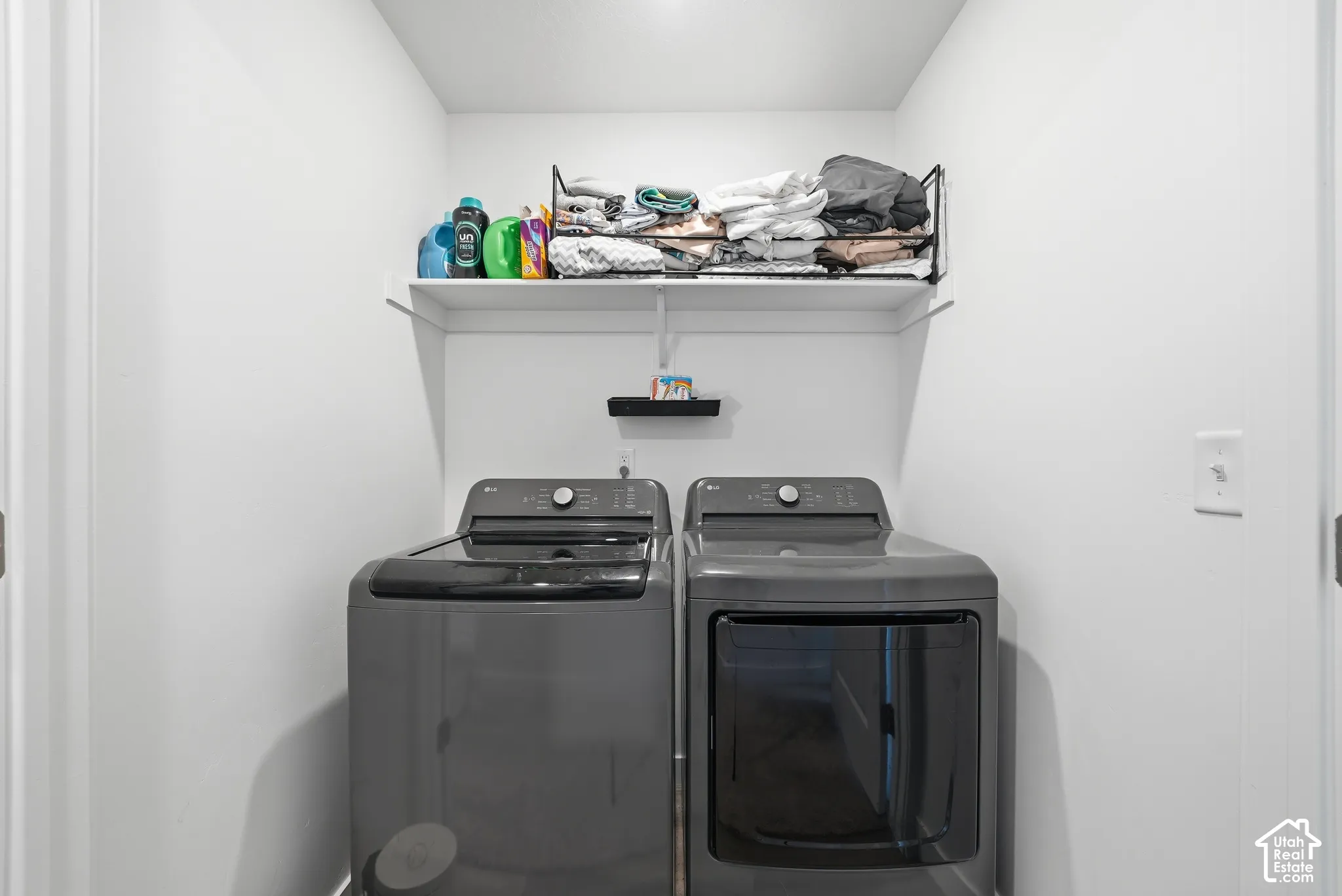 Laundry area featuring white walls, overhead wire shelving, and an additional wall-mounted shelf