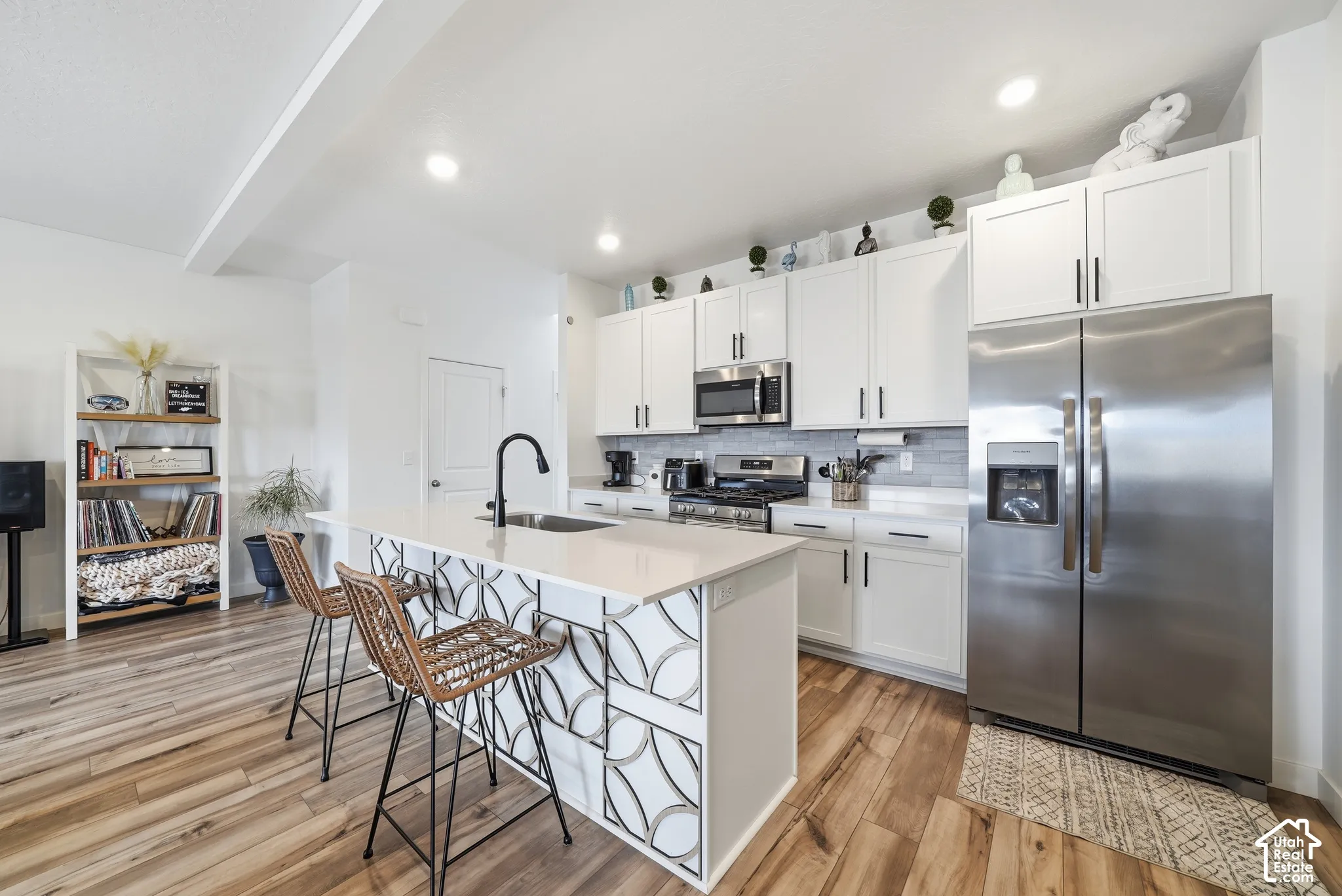 Kitchen featuring white shaker cabinetry, stainless steel appliances, quartz countertops, a decorative geometric-patterned island, and wood-finish flooring