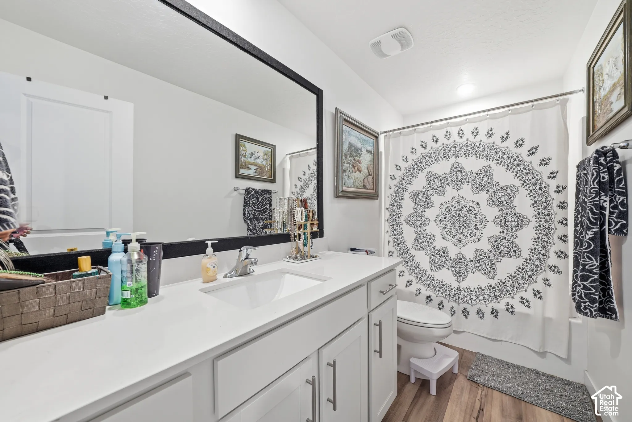Vanity with white cabinetry, solid surface countertop, integrated sink, and large mirror with a black frame, complemented by wood-finish flooring