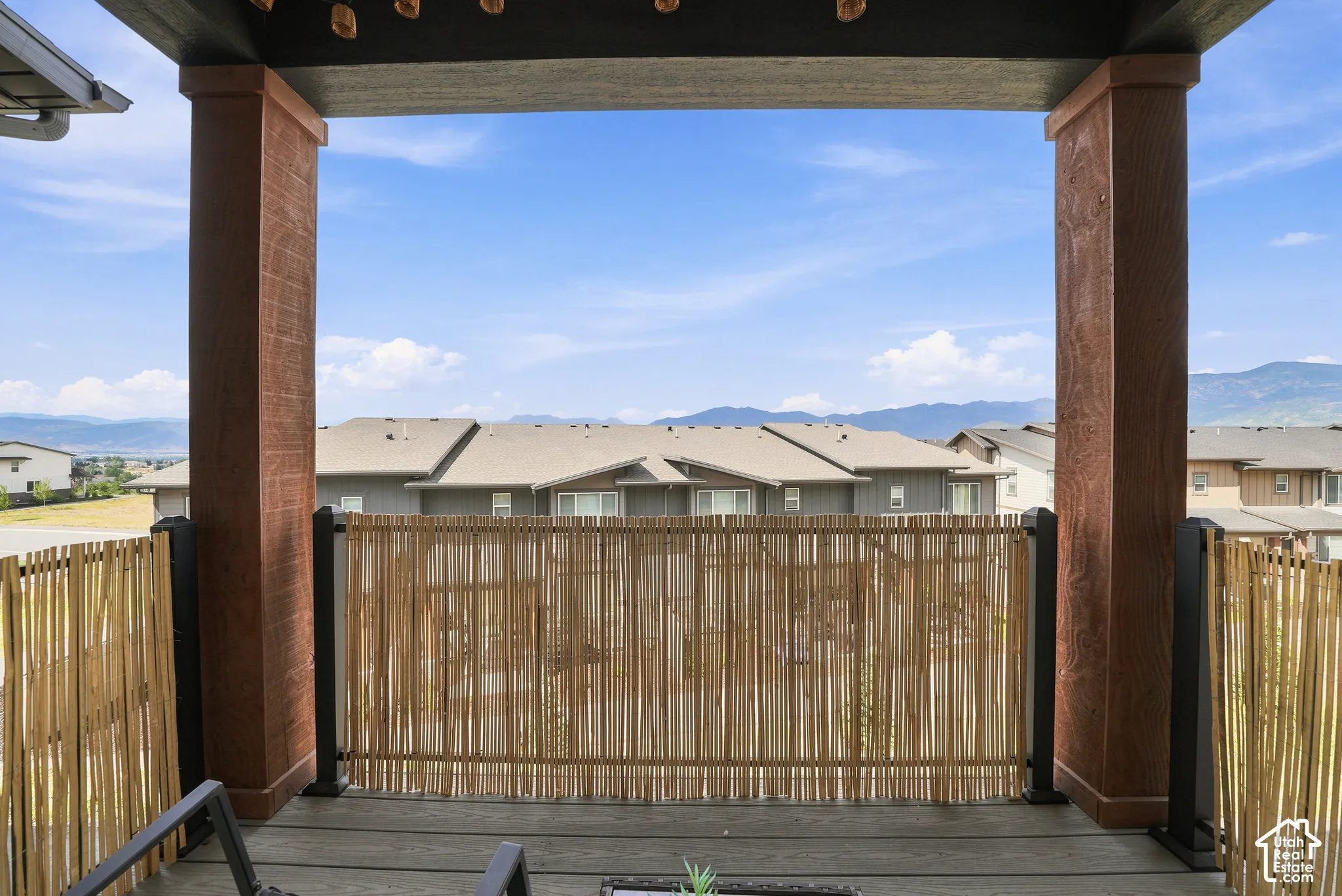 Covered outdoor balcony featuring wood-finish structural columns, natural reed screening, and mountain backdrops