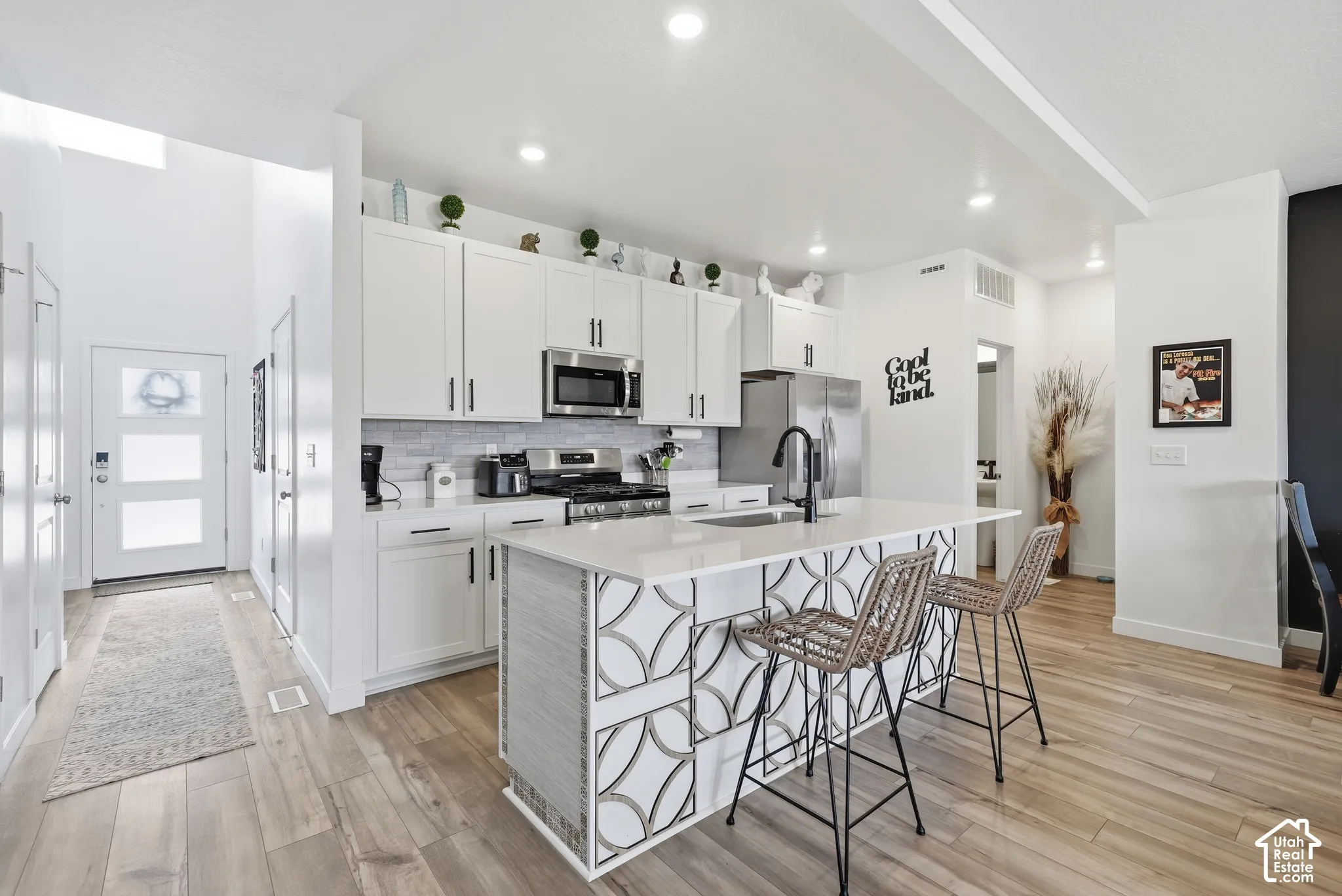 Kitchen featuring white shaker-style cabinetry, a central island with geometric decorative paneling, stone-surfaced countertops, stainless steel appliances, and wood-finish flooring