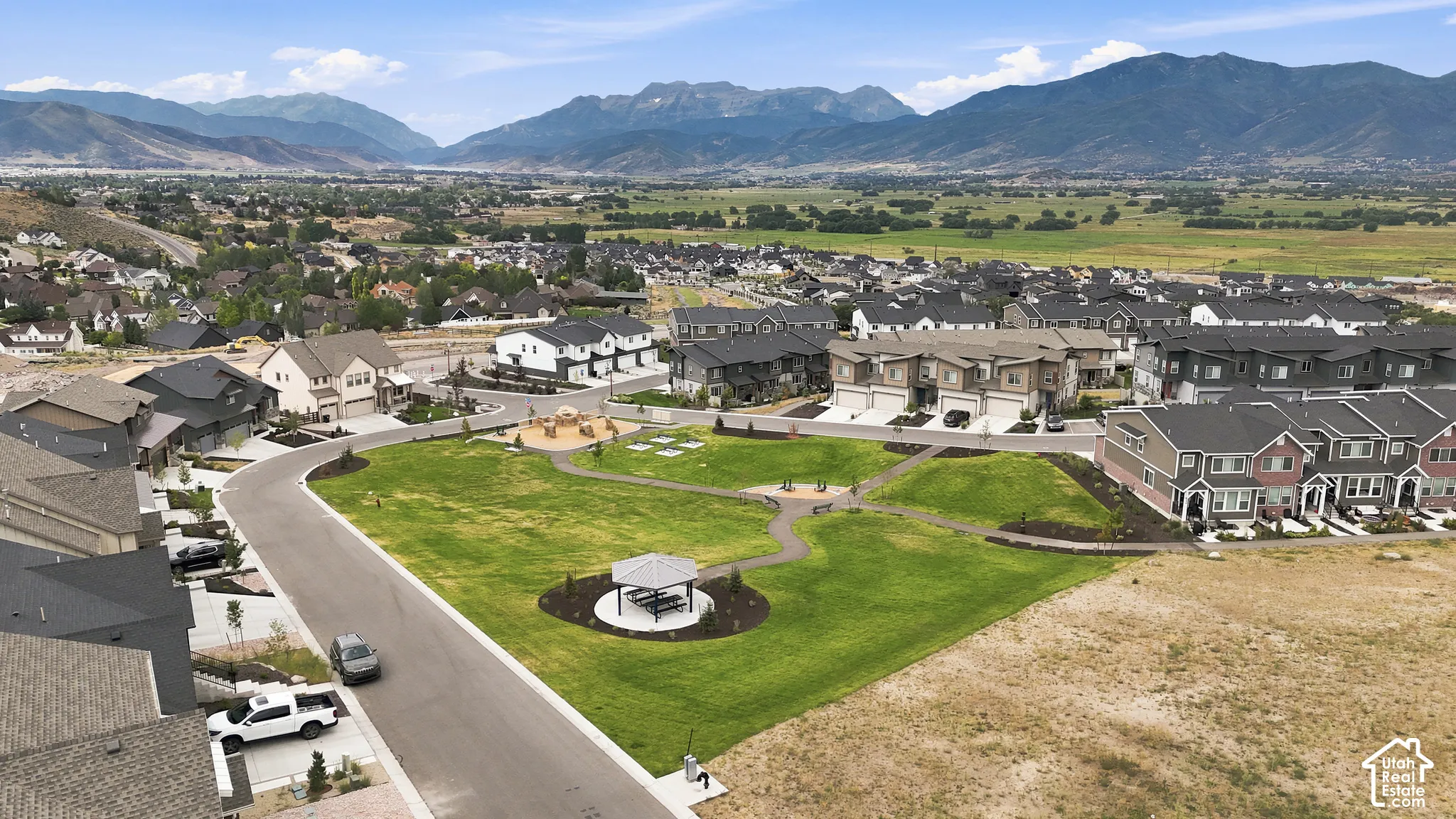 Aerial perspective featuring mountain backdrops, open green space, pedestrian pathways, a central gazebo, and a paved street grid